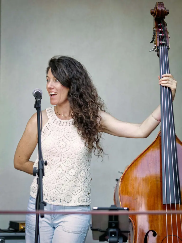Une musicienne aux cheveux longs chante au micro en tenant une contrebasse sur une scène