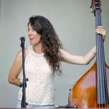 Une musicienne aux cheveux longs chante au micro en tenant une contrebasse sur une scène