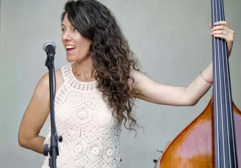 Une musicienne aux cheveux longs chante au micro en tenant une contrebasse sur une scène